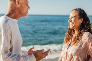 A happy elderly couple smiling and chatting at the sunny beach.