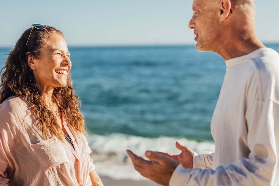 A happy elderly couple smiling and chatting at the sunny beach.